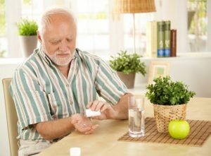 На фото: пожилой мужчина принимает таблетки